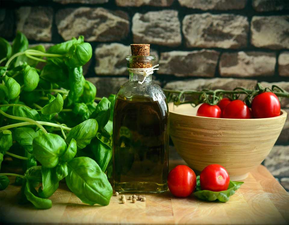 Olivenöl, Basilikum und Tomaten auf einem Holzbrett vor Steinwand
