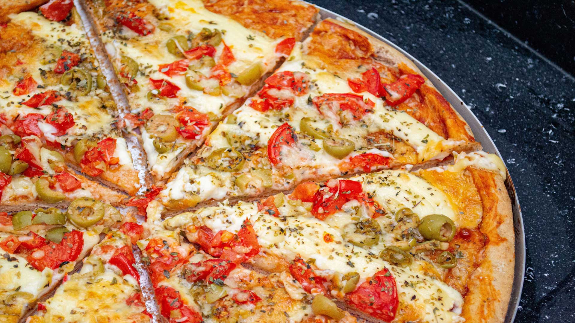 Aufgeschnittene Pizza mit Oliven, Tomaten und Käse