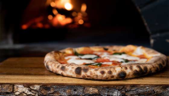 Margherita mit Basilikum vor dem glühenden Steinofen